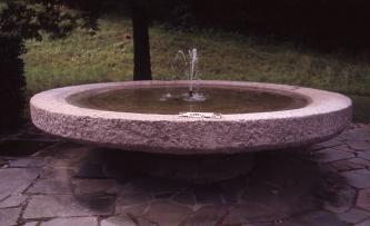 Die sogenannte „Suppenschüssel’“ am westlichen Ortseingang von Steinklingen. Das Bild zeigt einen schüsselförmigen Brunnen aus rosa Gestein. Der Brunnen ist wassergefüllt und in der Mitte befindet sich eine kleine Fontäne. Der Brunnen steht auf einer mit ebenfalls rosa Platten gepflasterten Fläche, im Hintergrund ist Wiese.