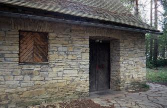 Blick auf eine Steinhütte mit Holztüren und hölzernem Fensterladen. Das Mauerwerk ist gelblich grau. 