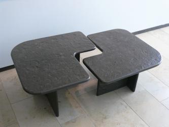 Zweigeteilter Steintisch mit abgerundeten Ecken und versetzten Innenkanten in J-Form. In der schwarzgrauen Tischoberfläche sind Fossilien erkennbar.