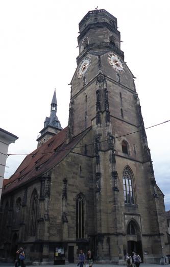Blick auf eine gotische, aus graubraunem Mauerwerk bestehende Kirche mit Eingangsportal, Hauptschiff und Kirchturm mit Galerien.