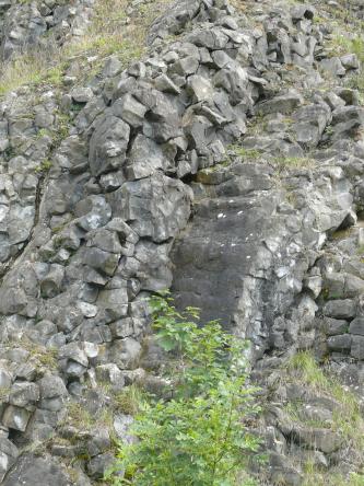 Auf diesem Bild liegen an einem Hang abwärts graue bis dunkelgraue Steinbrocken bogenförmig aufeinander und bilden dabei fast eine Art Rutschbahn.