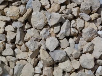 Nahaufnahme von bräunlich grauem bis leicht bläulichem Schotter. Die Steine sind rund oder eckig, mit scharfen Kanten.